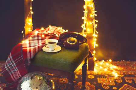 New Year's eve or Christmas still life with retro phone, disco ball, coffee, candle and blanket, golden backgroundの写真素材