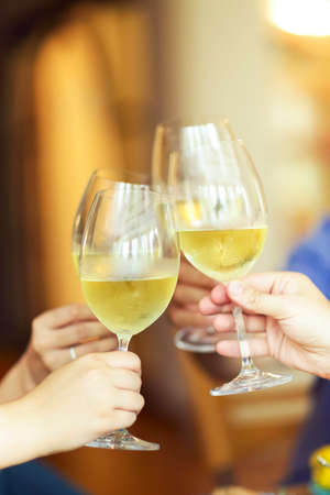 Group of people cheering with white wine and rising glasses on celebration at restaurant