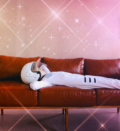 Astronaut futuristic kid girl with white full length uniform and helmet on the sofa. Dream, future, travel and discovery conceptの写真素材
