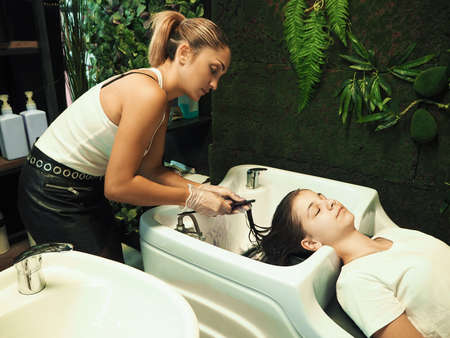 Cheerful young teen girl enjoying head massage while getting her hair washed by a professional hairdresser.  Beauty care, hairstyling, fashion, lifestyle glamour conceptの写真素材