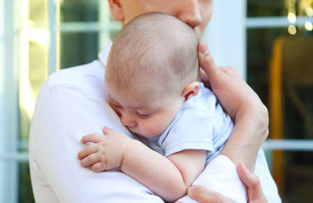 Close up portrait of young man holding adorable sleeping baby in his hands in the garden. Family, love and care conceptの写真素材