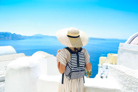 Young woman in a white dress and straw hat, walking at the city of Oia, island of Santorini, Greece. Concept of leisure, tourism, travel, vacations, romance, love 
の写真素材
