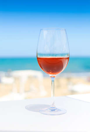 Glass of rose wine against blue water and sea in summer day