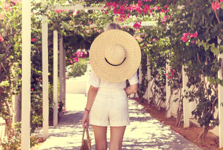 Blond girl in straw hat in front of pink bougainvillea flowers in sunlight の写真素材