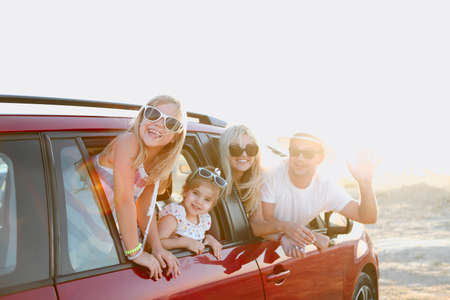 Happy smiling family with daughters in the car with sea background. Portrait of a smiling family with children at beach in the car. Holiday and travel concept 
の写真素材