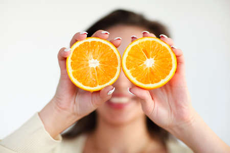 Portrait of the young brunette girl holding ripe orange isolated on light background