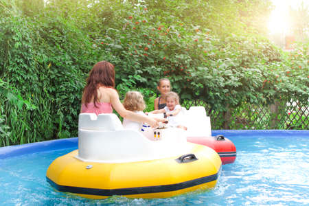 Adult woman with happy children riding colorful bumper boats near green bushes on sunny summer day in amusement parkの写真素材