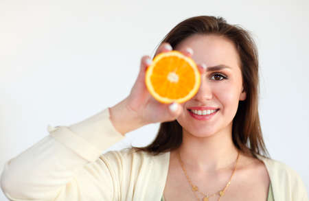 Portrait of the young brunette girl holding ripe orange isolated on light background