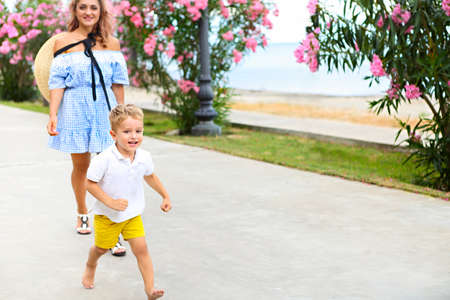 Young beautiful mother walking her little son outdoors. Mom and boy having fun together in green...