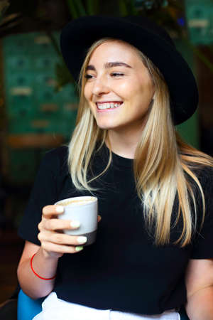 Happy young female with cup of fresh coffee smiling while sitting at table in street restaurantの写真素材