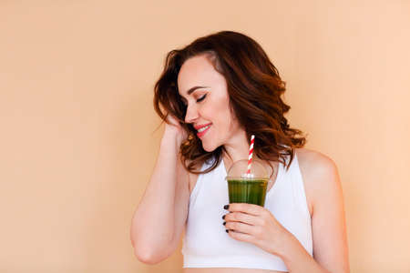 Crop delighted young woman with green smoothie laughing against wall backgroundの写真素材