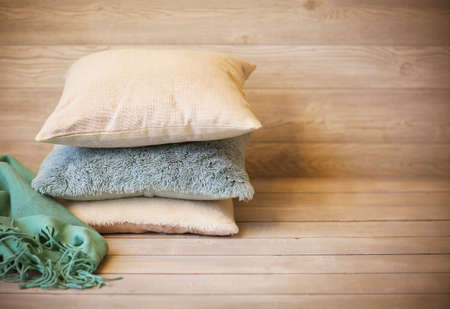 Soft cushions in light tones stacked with blanket on wooden shelf against wooden wall at homeの写真素材