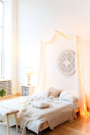 Comfortable canopy bed with soft pillows located in light minimalist bedroom in modern apartmentの写真素材