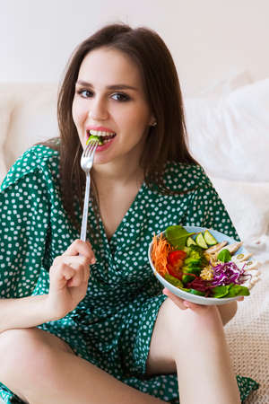 Young brunette girl bowl with healthy salad with vegetables and chicken meat
