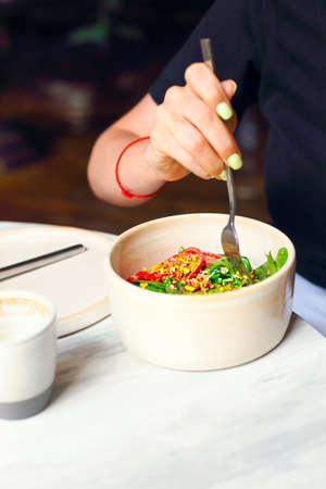 Crop hand of female sitting at round white table and eating delicious healthy fresh vegetable salad...