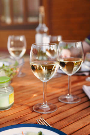 Glass goblets with white wine placed on wooden table during romantic dinner in yard