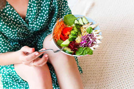 Top view of anonymous barefoot female in green dress showing bowl with healthy salad with vegetables and chicken meat. Close upの写真素材