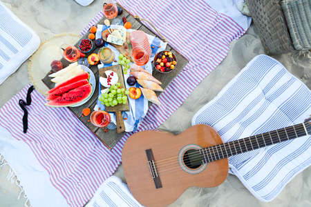Picnic serving pink wine having picnic with delicious snacks and fruit on sandy beach