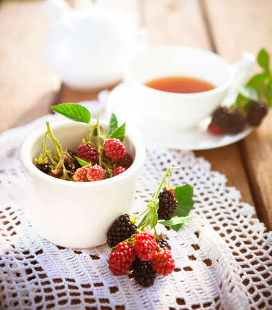 From above of fresh raspberry and blackberry with green leaves on wooden table with white knitted...