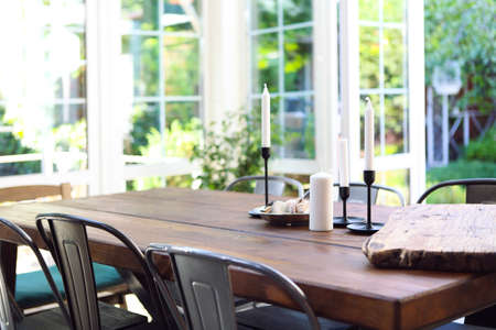 White candles and plate with snacks placed on wooden table on glass terrace on sunny summer day in...