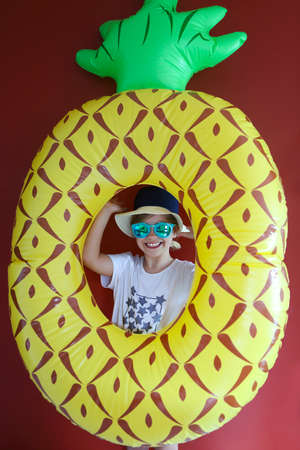 Pretty emothional child wear a hat and sunglasses holding swiming float ready to swimm on a red...