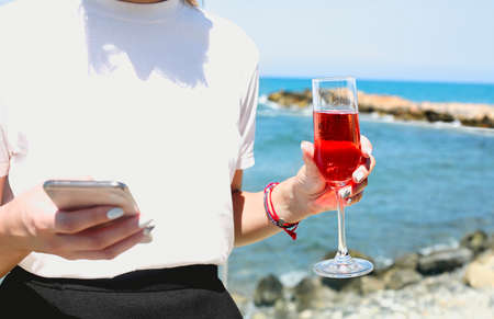 Relaxed young female in casual wear holding glass of rose champagne and holding mobile phone...