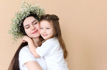 Young brunette mother and little daughter stand near the wall with big flowers wreath. Mother's day conceptの写真素材