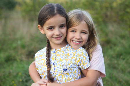Portrait of the happy blond and dark haired girls sisters laughing and hug in sunsetの写真素材
