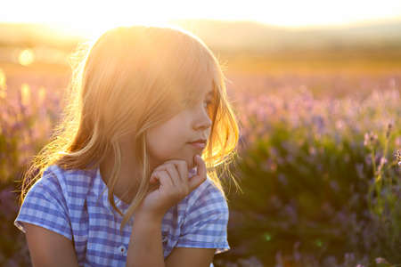 Portrait of the happy little girl blonde with long hair at sunset in lavender fieldの写真素材
