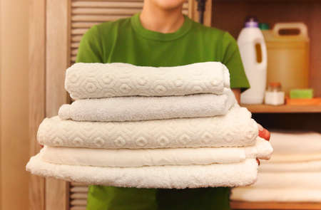 Cropped view of the woman wearing green t-shirt near cupboard holding towels in laundry room. Cozy and clean house conceptの写真素材