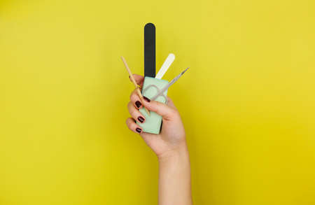 Unrecognizable female with painted nails showing bunch of various manicure tools against bright...