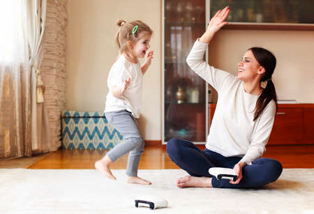 Delighted woman and girl with gamepads smiling and doing high five while sitting cross legged on floor and playing video game together at homeの写真素材