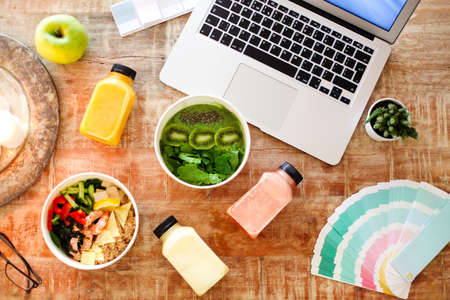 Top view of bowls with healthy dishes and bottles of smooties placed on table near laptop and palette samples during lunchの写真素材
