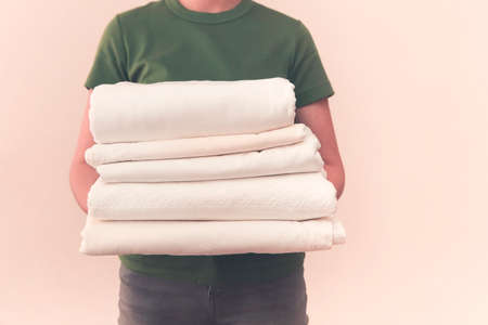 Young woman wearing green t-shirt holding towels in laundry room. Cozy and clean house concept