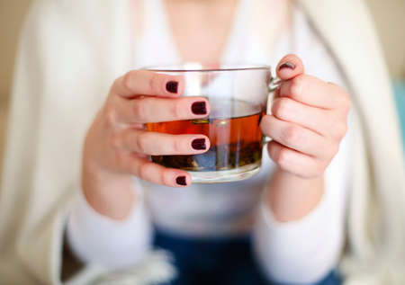 High angle of crop female in casual outfit holding glass cup with aromatic herbal tea while relaxing at homeの写真素材