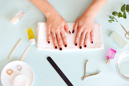 Top view of crop anonymous female with dark manicure sitting at table with various tools during...