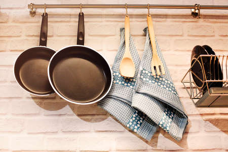 Stainless railing with frying pans and wooden utensils with towels above counter with brick wall in kitchenの写真素材