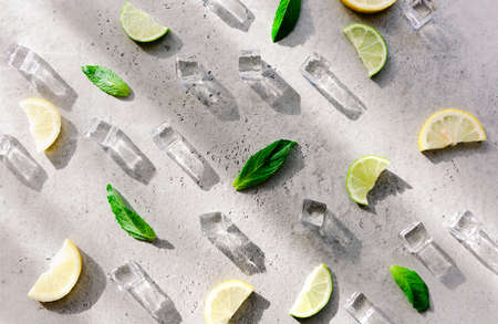 Fresh mint leaf and ice cubes with droplets and lime on cement background. Summer backgroundの写真素材