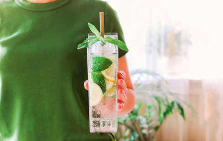 Young woman holding fresh lime, lemon and mint infused water, cocktail, detox drink, lemonade in reusable bottlesの写真素材