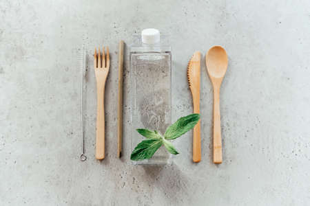Top view of eco friendly utensils placed near bottle with water and mint leaf on gray stone surfaceの写真素材