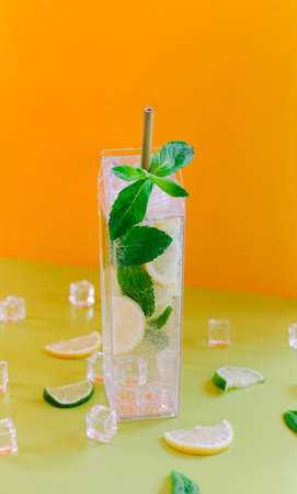 Tall glass of cold mojito drink with citruses and mint leaves placed on green table against orange backgroundの写真素材