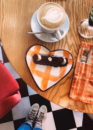 From above of crop anonymous female standing at table with delicious sweet dessert and cup of cappuccino in cafeの写真素材
