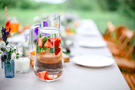 Glass jug of fresh water with mint and strawberries placed on table on terrace for breakfast in morningの写真素材