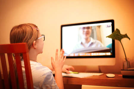 Back view of anonymous girl raising arm while sitting at desk and attending online lesson at home