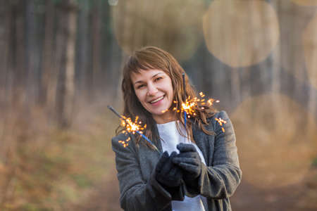 Smiling and happy pretty woman enjoying bengal light among winter forestの写真素材