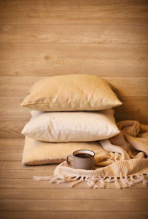 Cozy background with pillows and cup of beverage against blurred wooden wall as symbol of warmth and comfort at homeの写真素材