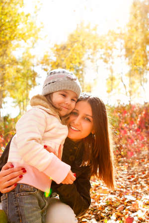 Cheerful woman smiling and hugging delighted girl while spending time in autumn park togetherの写真素材