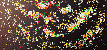 Top view of multicolored confetti scattered on navy blue background during party in studio