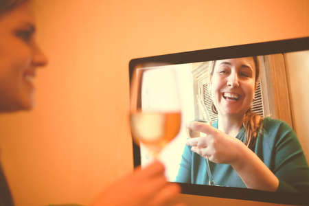 Content female friends with wineglasses communicating via video call and drinking alcohol beverages together during coronavirus epidemicの写真素材