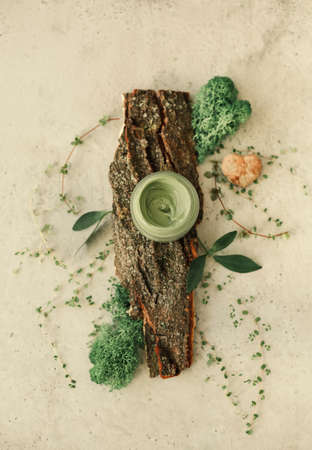 Top view of natural green clay mask in glass jar arranged on table with fresh plants
